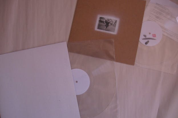 Clear records slipping out of their casing photographed against a bed sheet. 