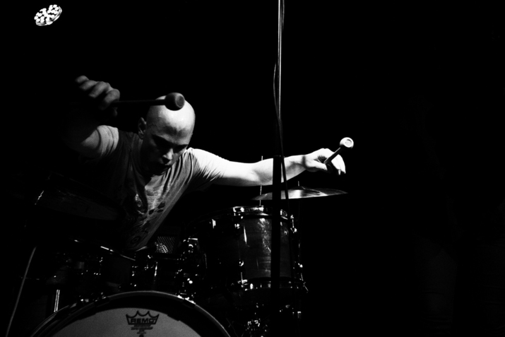 Black and white photograph of person leaning forward on top of drums.