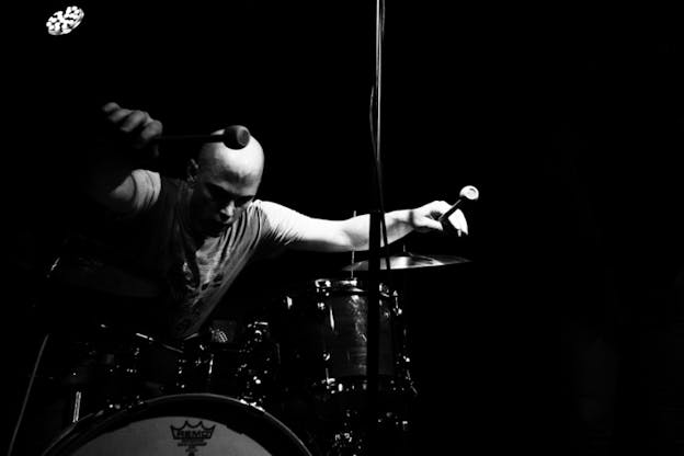 Black and white photograph of person leaning forward on top of drums.
