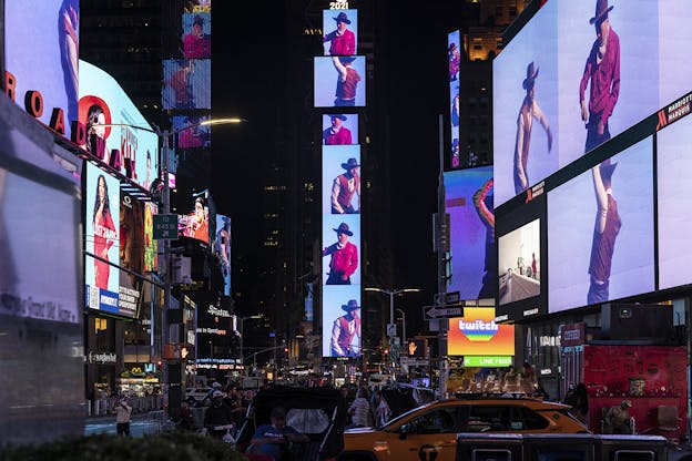 Videos of performers wearing cowboy hats, red shirts, bandanas and brown vests are projected onto large screens in Times Square.