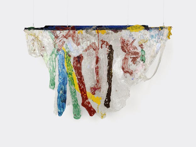 A hanging sculpture of primarily opaque white acrylic draped over a thin plank of wood that is painted dark blue. Stripes of green, blue, yellow, red, and brown run vertically along the draped white acrylic, resembling drips. Areas of red and yellow and speckles of blue appear throughout other areas of the piece. The bottom edges of the draped acrylic are smooth and sloping.
