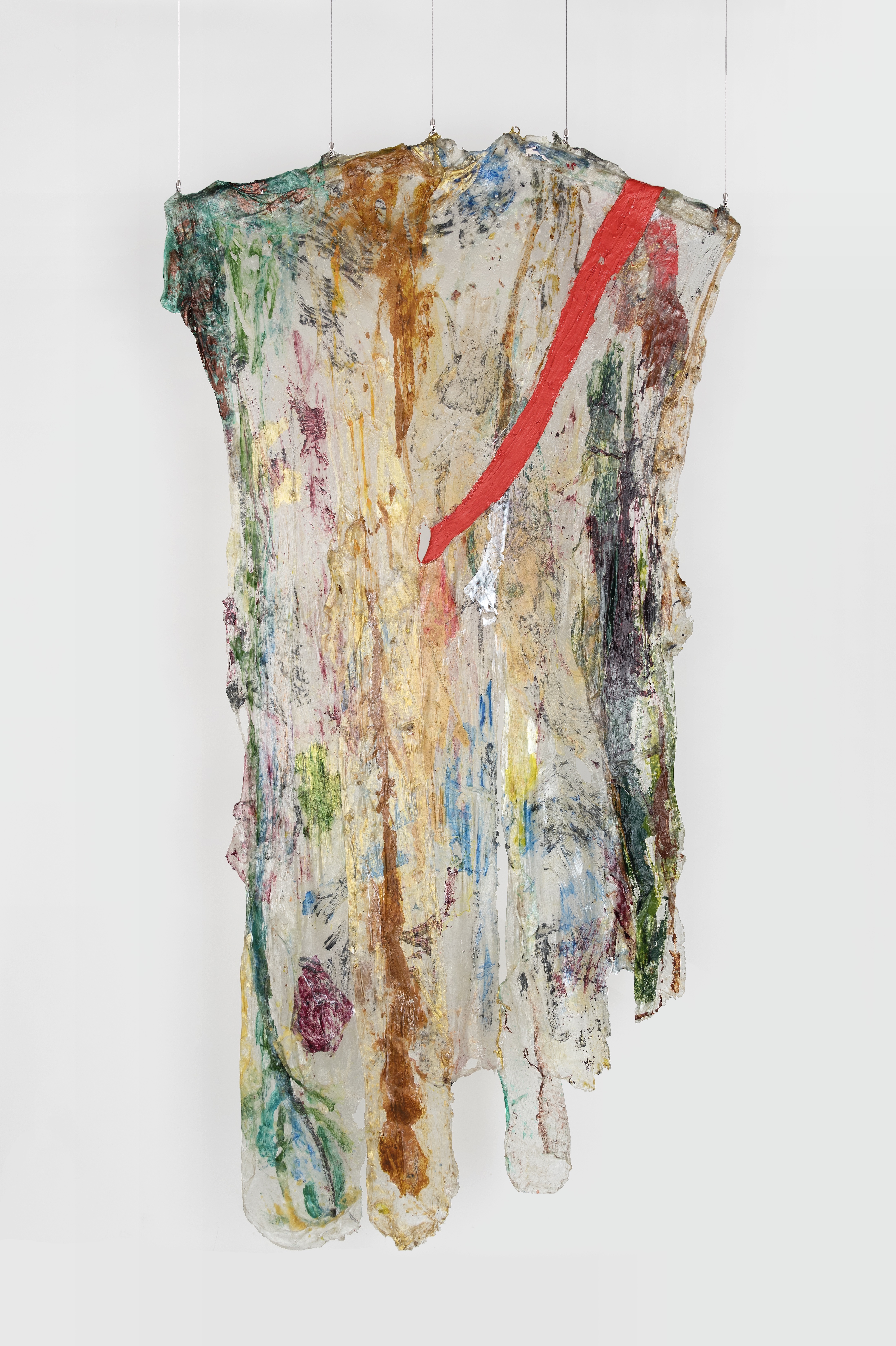 A hanging sculpture made of transparent plastic draped over two, short wooden rods, with painted areas. The rods are tilted slightly, resembling the arms of a clothes hanger. The plastic ends are cut in rounded forms. Dark green, red, brown, and magenta paint areas are visible on the plastic. A strip of red plastic starts at the top right and drapes across the face of the transparent piece, the bottom end coming through a hole in the center of the piece towards the back. 