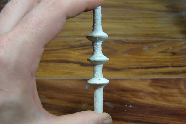 Close-up of three fingers balancing a screw painted in clumpy white paint. 