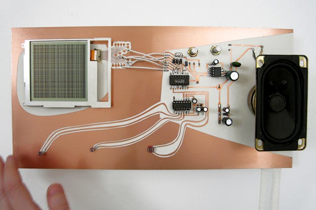 A rose gold motherboard with a square green device on the left side and a rectangular black device on the right, on top of a white surface.