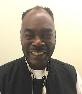 A portrait of Frederick Weston dressed in a white sweater, black sleeveless vest and a short black and white scarf with smiley faces. 