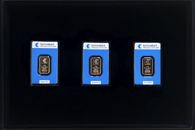 Three aligned gold bars inside plastic covers with blue and white paper background on their top typed: 