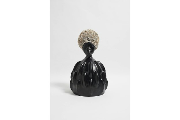 A small black statue of a figure with a round bottom under the neck, with almond shaped textures. On the head of the figure colorful rose buds cover the whole surface.