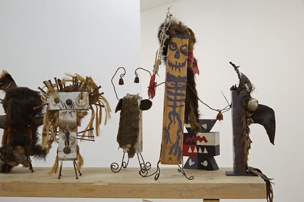 Small figurines with wires as legs and hands, straw and fur hair, ominously drawn faces and skeletal bodies on wood.