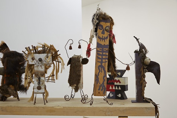 Small figurines with wires as legs and hands, straw and fur hair, ominously drawn faces and skeletal bodies on wood.