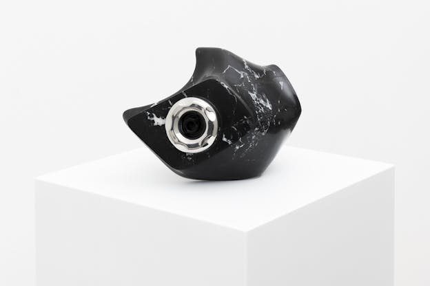 A black with white marbled ball size sculpture with various indentations and smooth peaks on the surface holds in its middle a silver and black jacuzzi valve. 