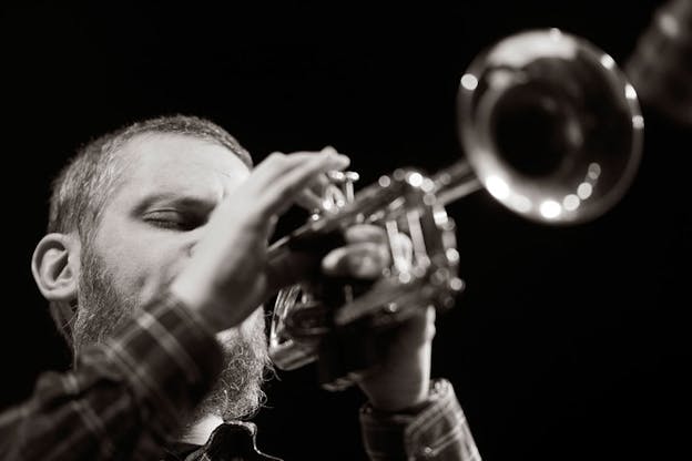 Black and white photograph of Wooley closing his eyes and playing the trumpet. Wooley's face is focused while his hands and the trumpet are blurred.