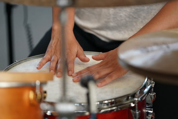 A close up photograph of Susie Ibarra's two hands placed lightly on top of an orange drum. 