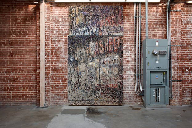 Abstract wall length painting of various dots swipes of colors and writing sits in the middle of a red brick wall. To its right a gray electric panel.