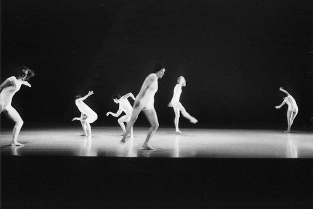 Multiple performers in white are on stage in various movements.