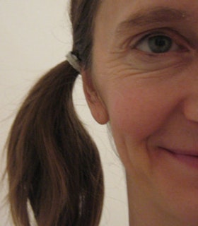 A close up portrait of Kimberly Bartosik against a white background. Only half of her face and one of her pigtails is visible.