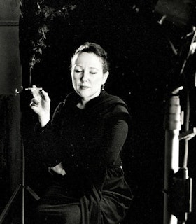 Black and white portrait of Black-Eyed Susan poised with an all black outfit and a lit cigarette in their hand.