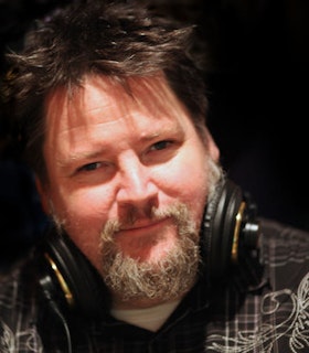 Close up portrait of Jim Findlay with a grey beard and short brown hair. Headphones frame his face.