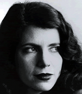 A close up, black and white portrait of Annie Gosfield looking towards the right. She has curly, shoulder length black hair and is situated in front of a white background. 