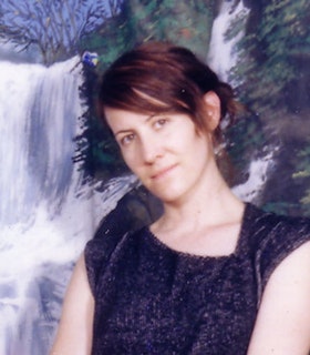 A portrait of Stuart Hawkins against a waterfall wallpaper. She wears a sleeveless black shirt and tilts her head to the left.