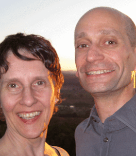 Portrait of two Every house has a door members smiling at the camera. On the left, Lin Hixon has short hair. On the right, Matthew Goulish is bald and wearing a grey polo shirt.