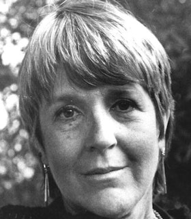A black and white close up portrait of Joanne Kyger smiling slightly in front of a blurred, spotted background. She has short hair with bangs.