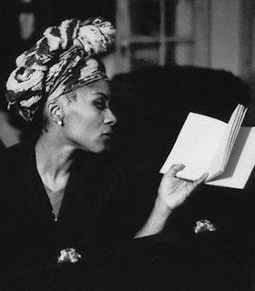 Black and white profile of Julie Patton wearing a patterned head wrap and holding a book.