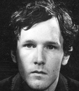 A close up, black and white portrait of Guido van der Werve in front of a black background. He has short hair and looks directly at the camera. The image itself is lightly scratched. 