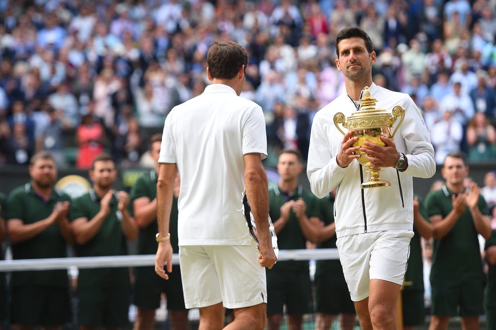 Novak Djokovic passing by Roger Federer with his trophy at Wimbledon 2019