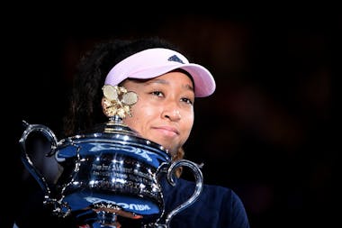 Naomi Osaka psing in the light and smiling with her 2019 Australian Open trophy