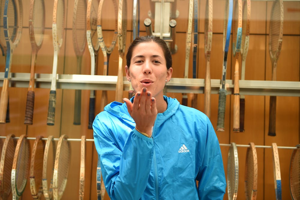 Garbine Muguruza smiling and kissing away the camera in front of vintage raquets at Roland-Garros