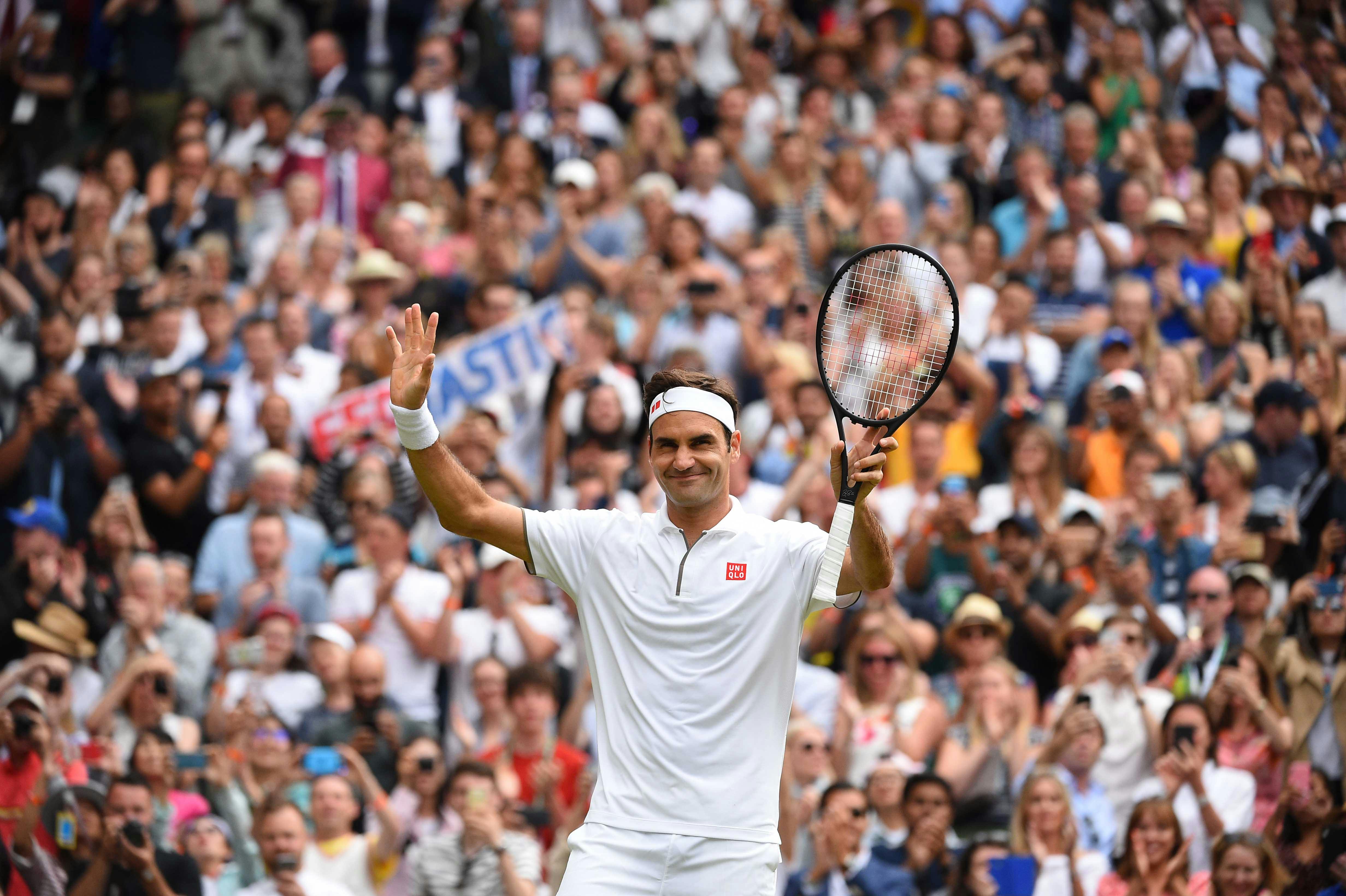 Roger Federer smiling while waving to the crowd after his third round victory at Wimbledon 2019.