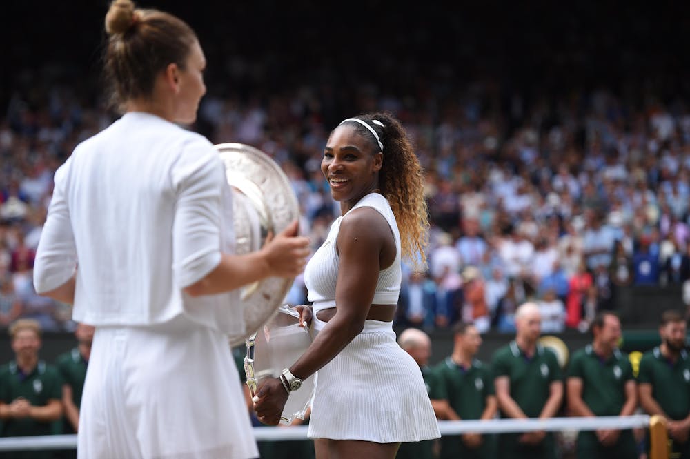 Serena Williams  looking smiling at Simona Halep and her Wimbledon 2019 trophy.