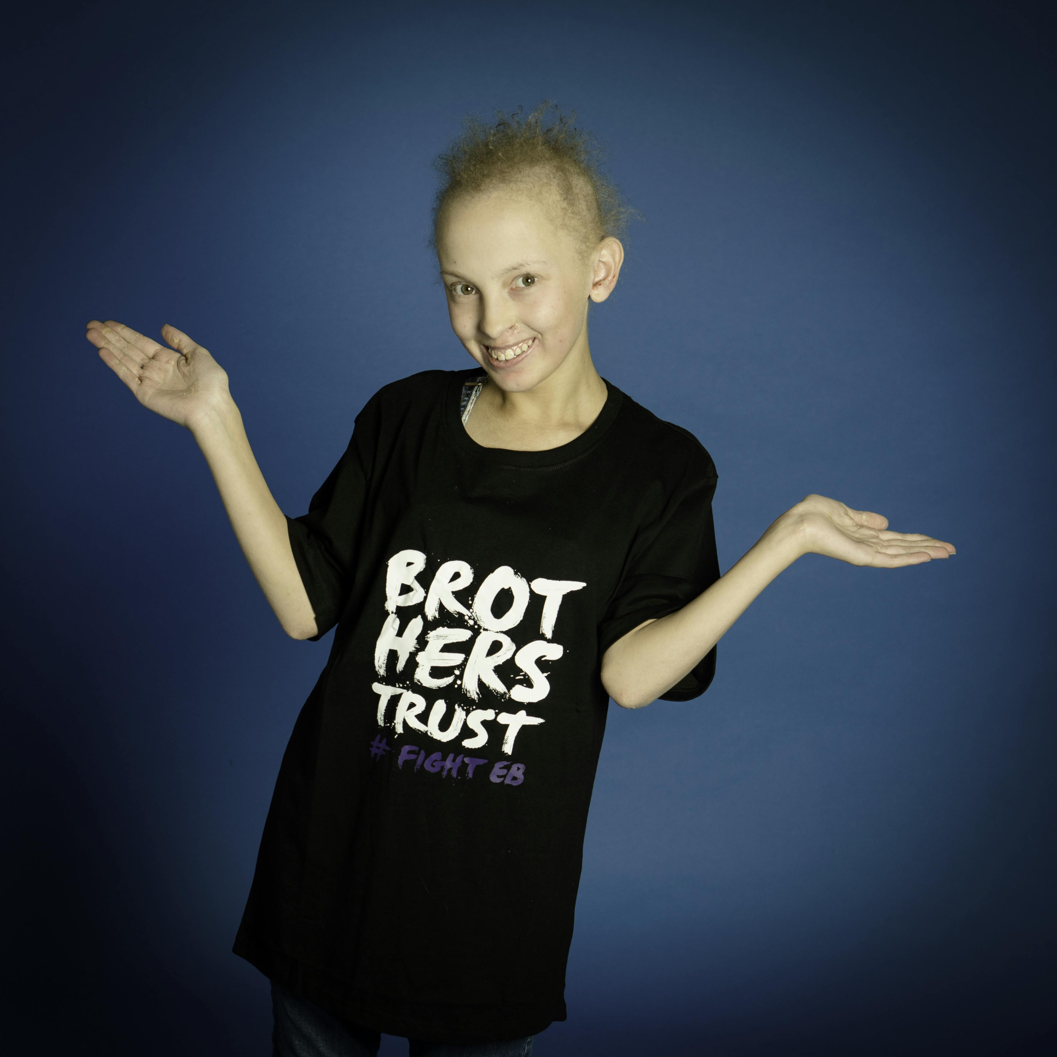 A girl in a black t-shirt shrugging with her arms wide apart and hands splayed, smiling at the camera.