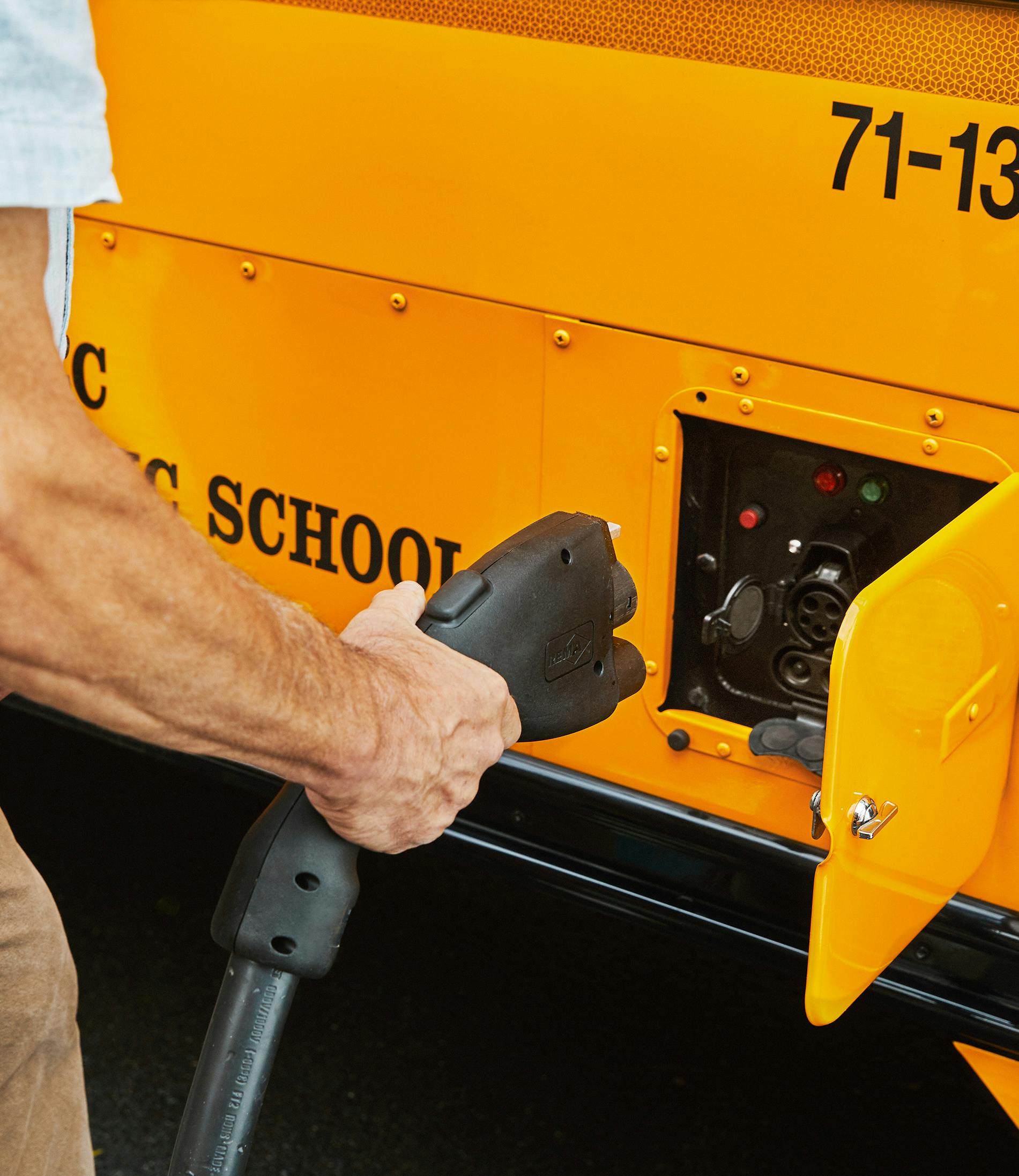 A man plugs in the charger for the Highland electric school bus.