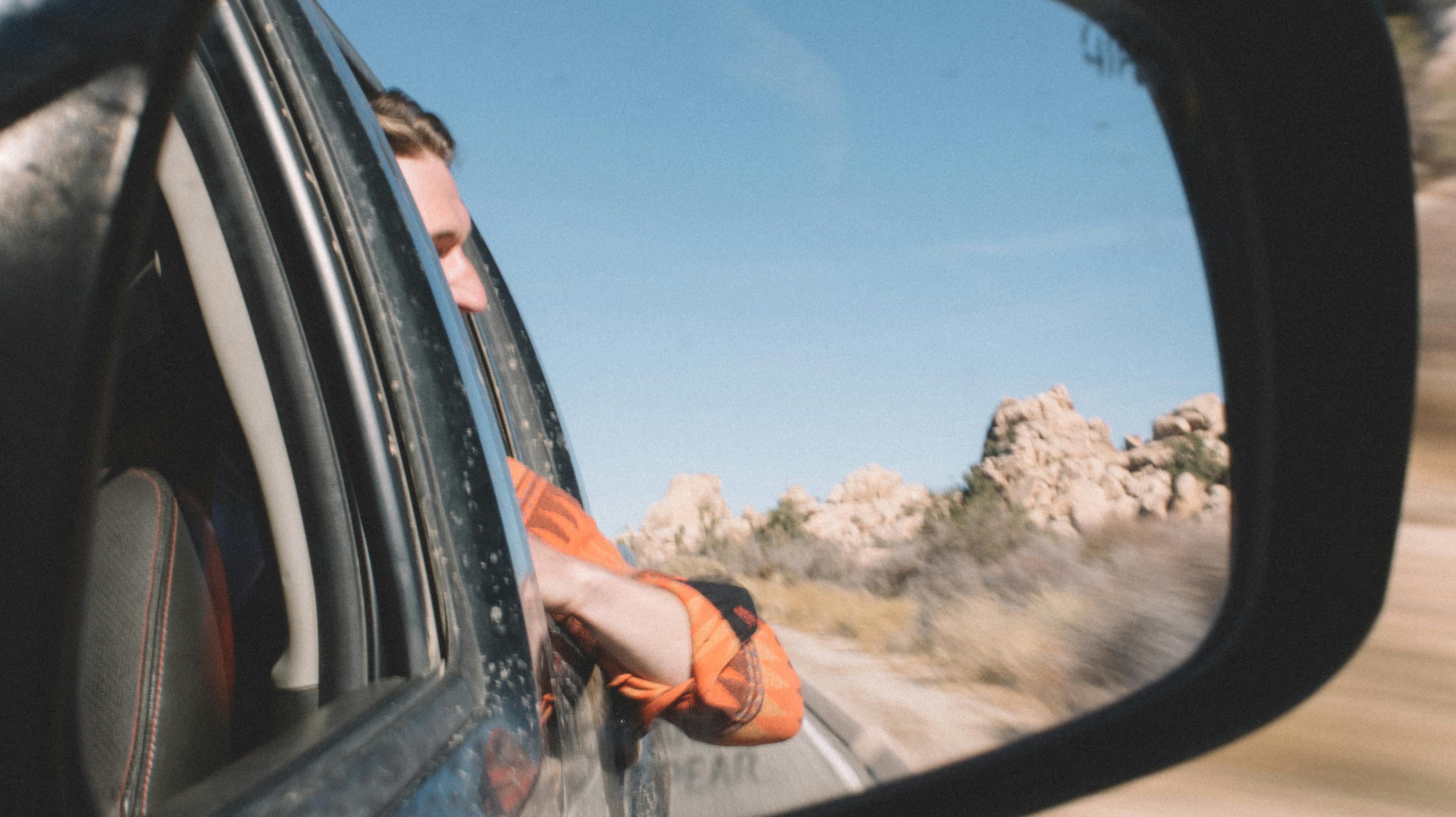 The reflection of a young man shot from a car's sideview mirror as they drive down the highway in Southern California.