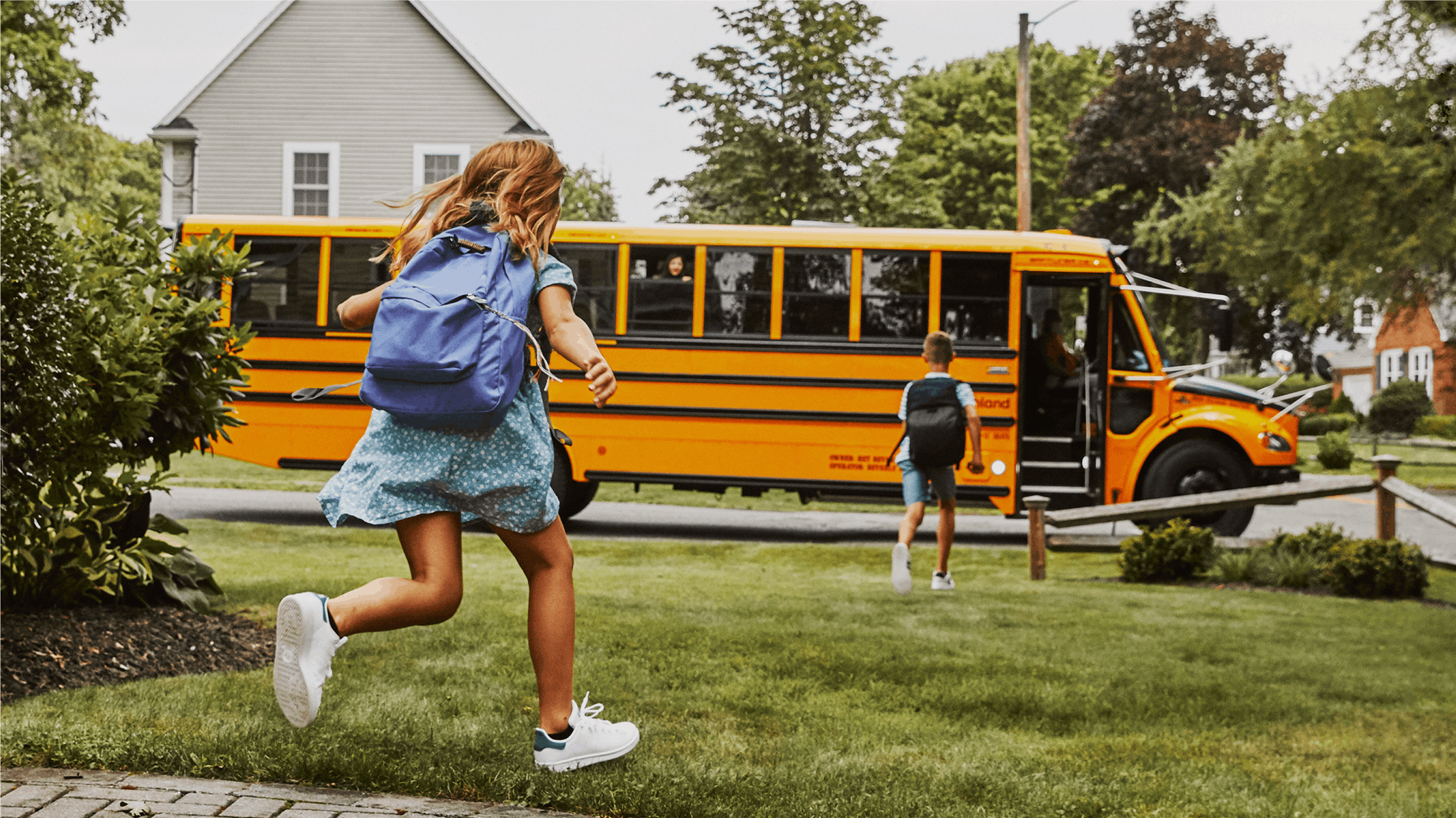 Two kids run through their yard to get on the Highland electric school bus.