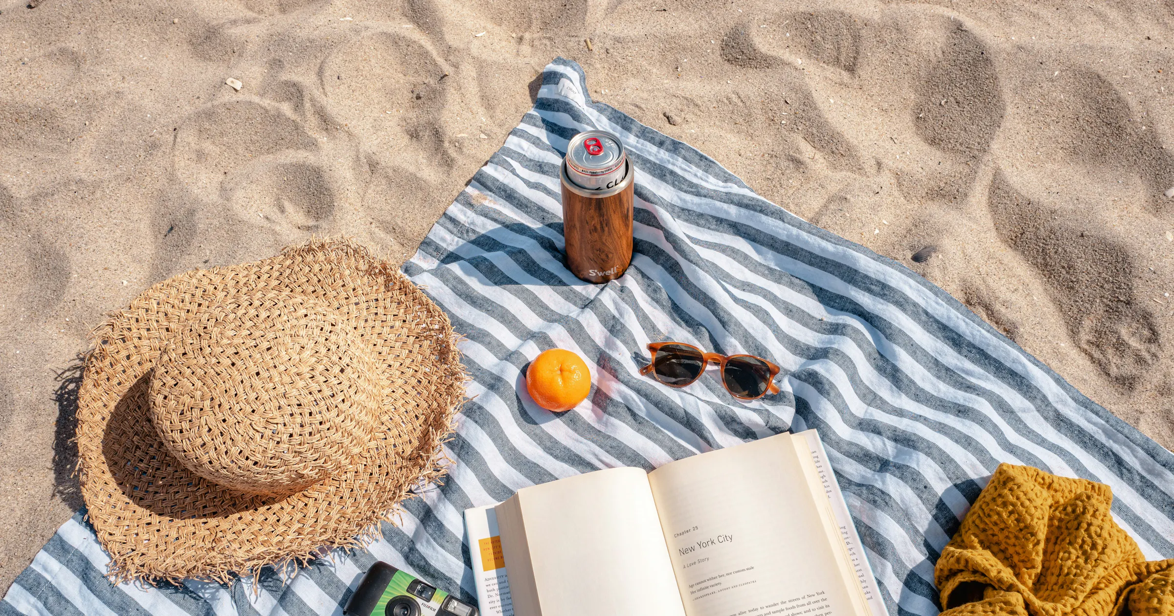 toalha de praia na areia com chapéu, bebidas e livro