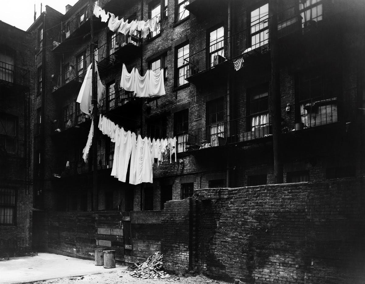 Black and white photograph of tenement housing, with laundry lines strung between balconies. 