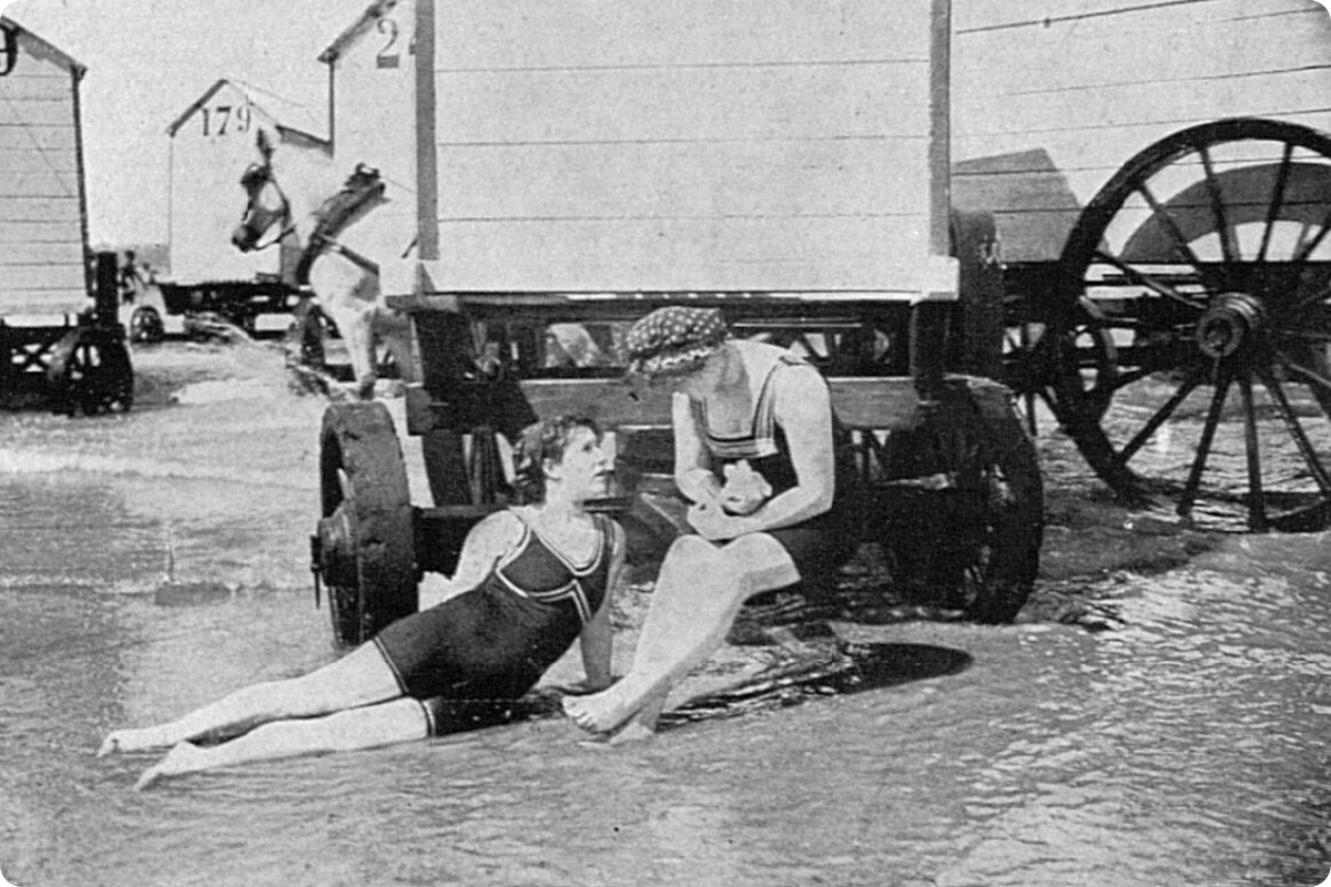 Vintage photo of women and bathing machines at the beach.