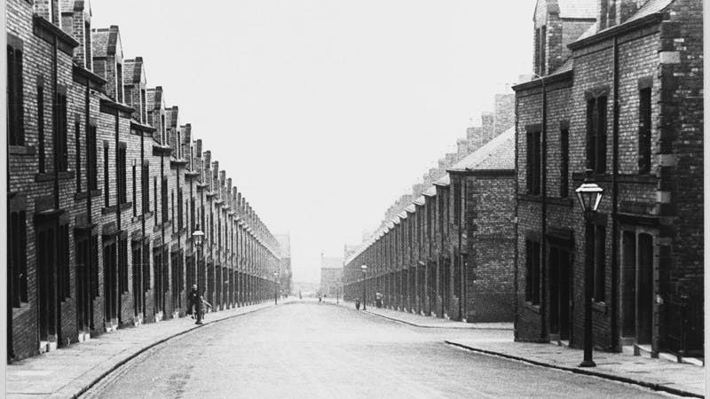 Black and white photograph looking down a street of terraced houses in the 1930s.