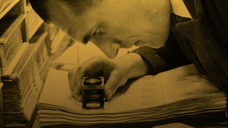 A photo with a yellow tint of a man using a magnifying glass to read old documents from the 1939 register
