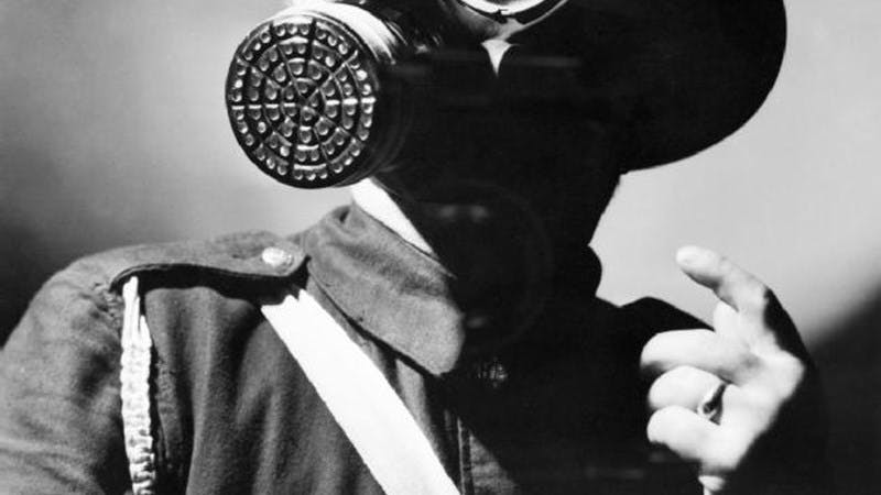 Black and white photo of an Air Raid Warden in uniform, wearing his steel helmet and duty gas mask.