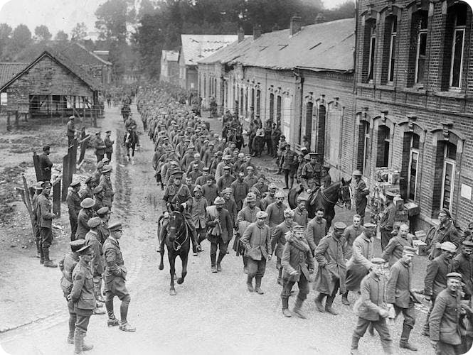 Canadian troops march prisoners through a town, c.1918.