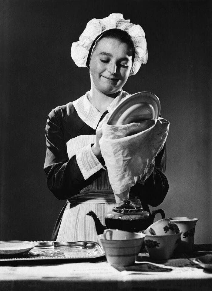 A black-and-white photograph of a maid cleaning a plate.