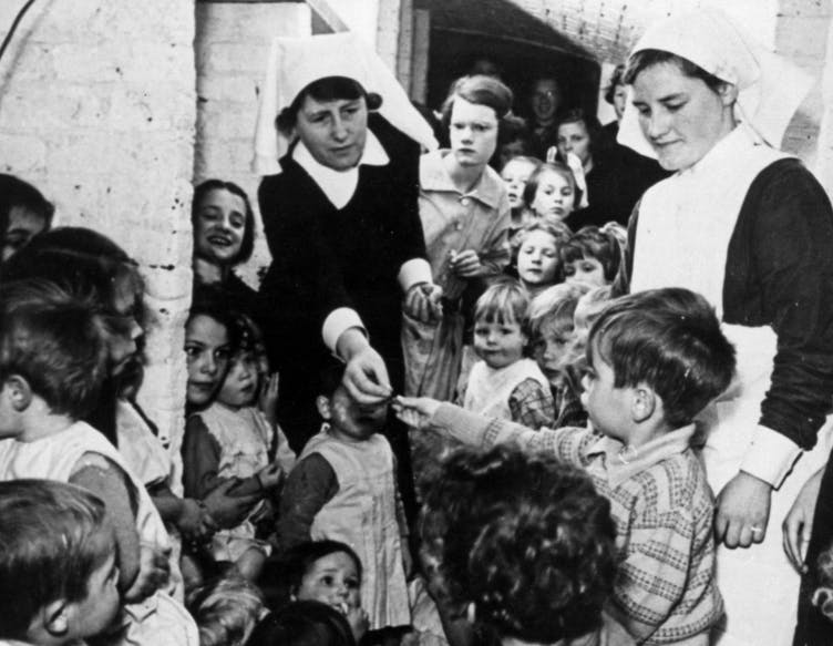 A nurse distributes sweets to children in a shelter, 1939, from the Findmypast Photo Collection.