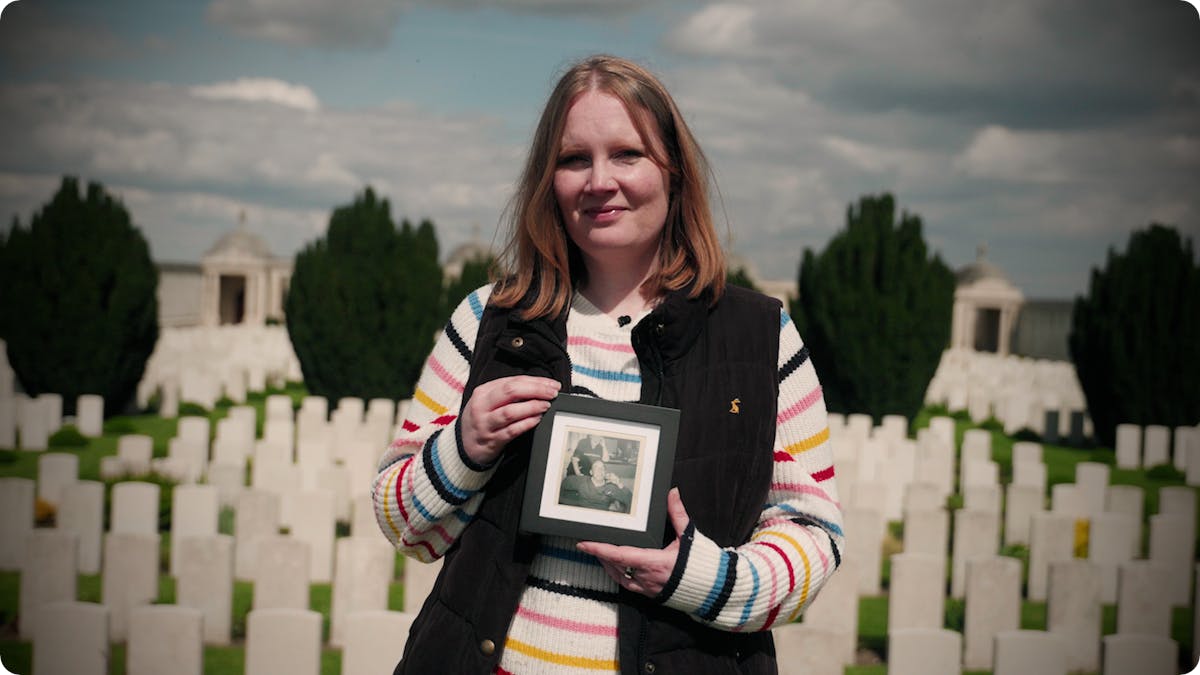 Laura holding a photo of her great-grandfather Eli, in front of graves at Loos Cemetery in France.
