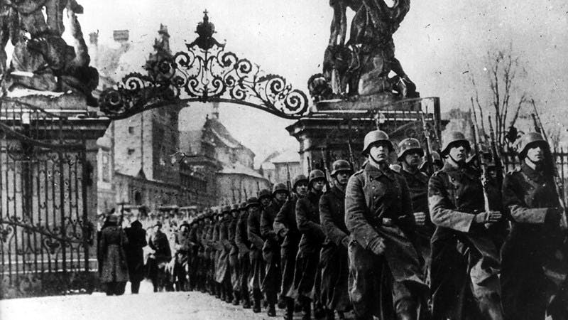 Black and white photograph of soldiers marching through an iron gate.