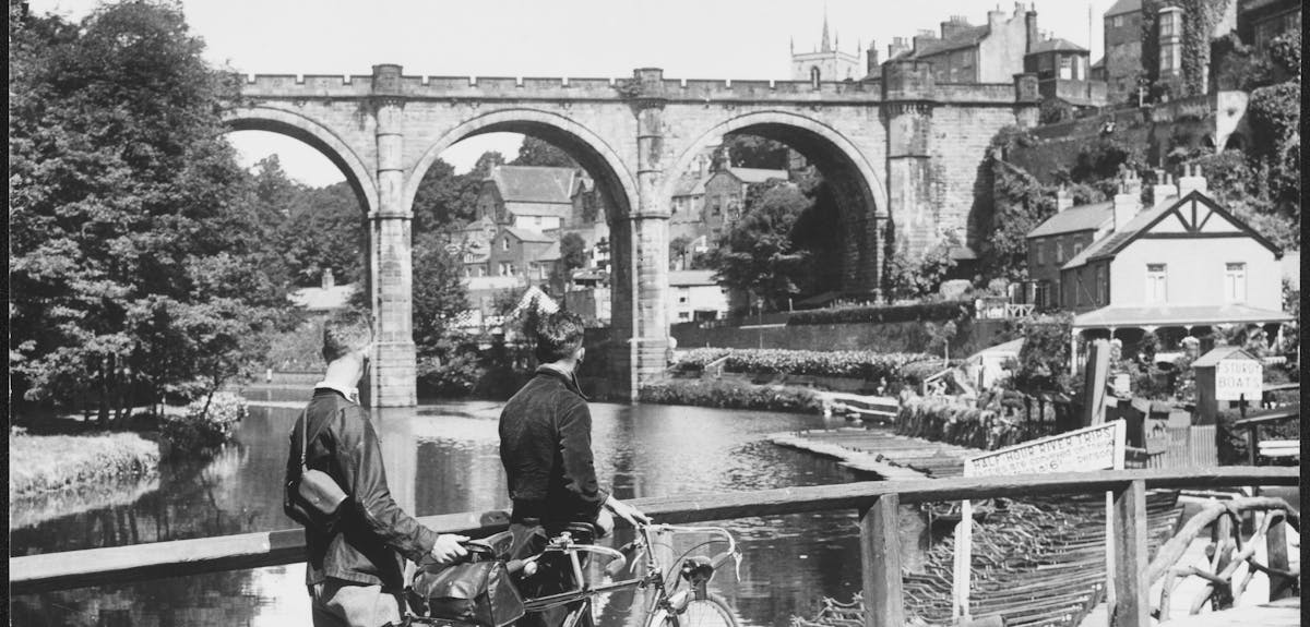 Two men with bicycles looking at a bridge crossing a river.