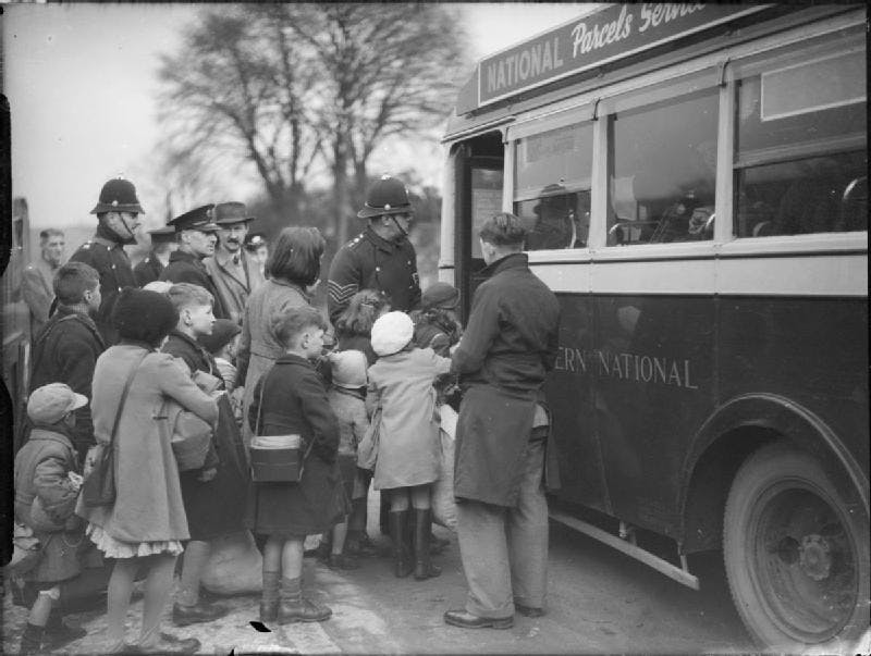 A black and white photograph of children being helped on to a bus by policemen. 