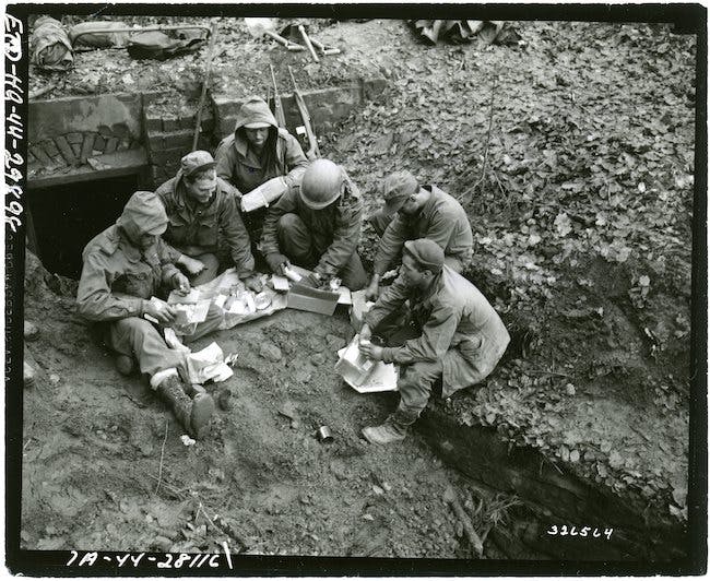 Infantrymen of Company C, 2nd Bn., 389th Regt., 100th Div., open Christmas boxes while they are waiting for orders to attack the Maginot line. Bitche area, France. 15 December 1944. U.S. National Archives.